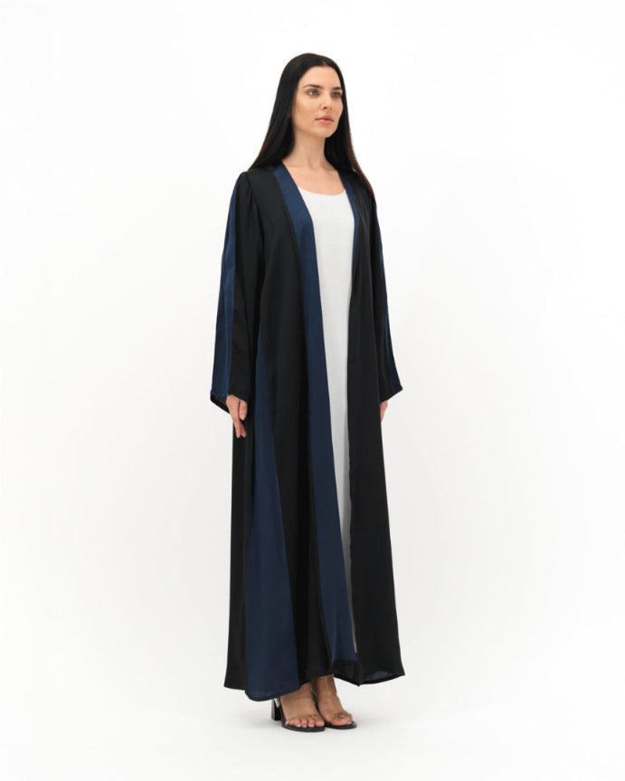 Woman wearing a long black and navy abaya over a white dress on a white background