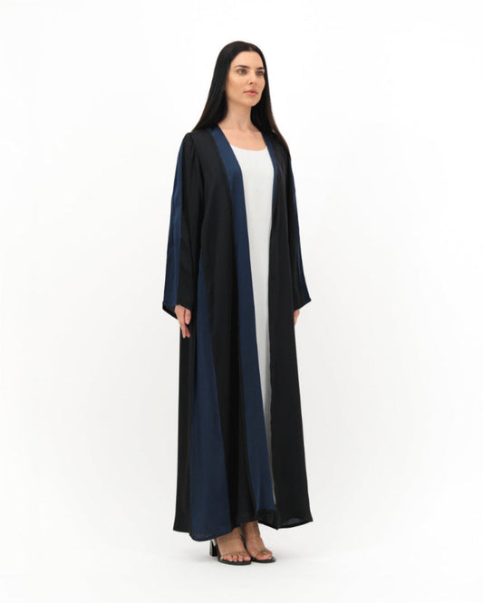Woman wearing a long black and navy abaya over a white dress on a white background