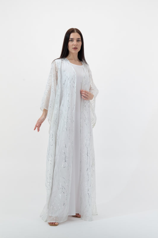 Woman wearing a long, light-colored dress with sheer sleeves against a white background